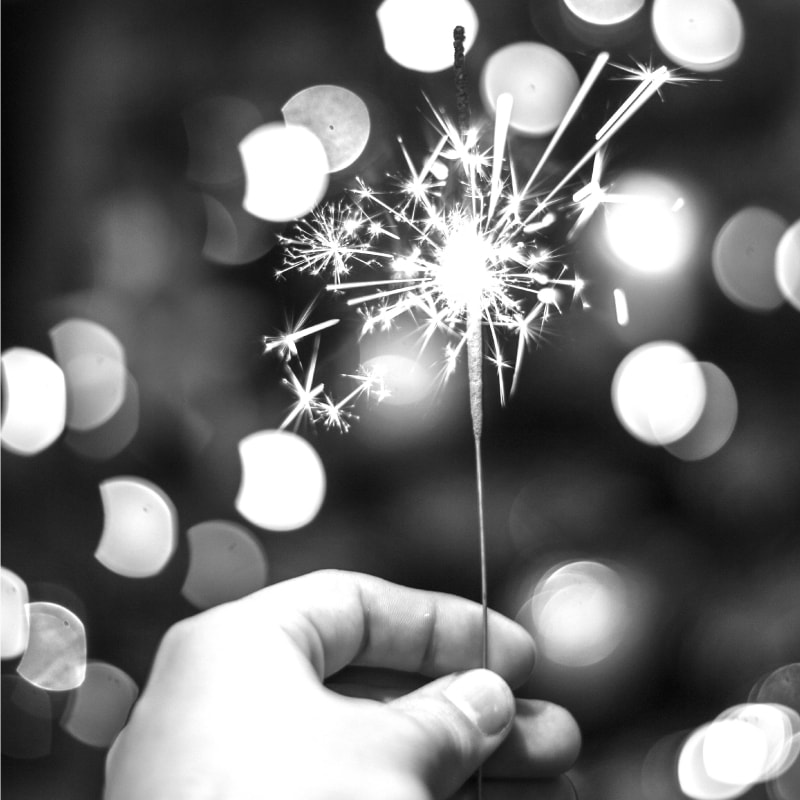 A black and white image of a hand holding a lit sparkler