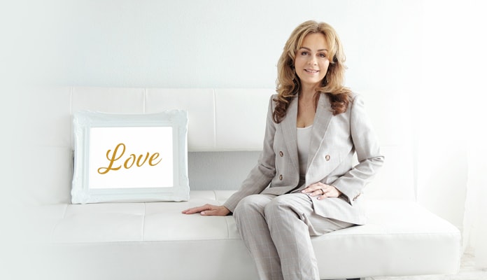 Lisa Thomas sitting on a white couch next to a frame with the word Love in it.