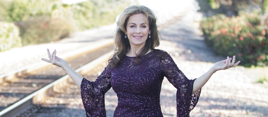 Lisa Thomas wearing a dark purple dress with arms in "W" shape, standing next to railroad tracks