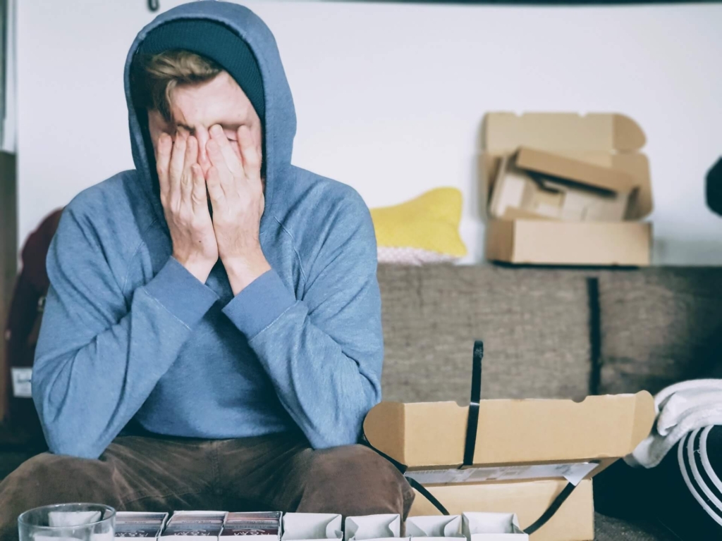 A man who looks anxious, covering his face with piles of stuff around him.